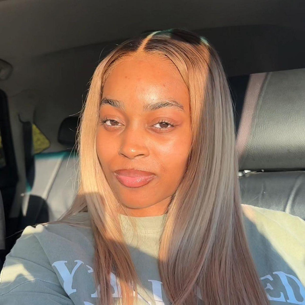 Black woman with dark roots, blonde wig, long, straight hair sitting inside a vehicle

